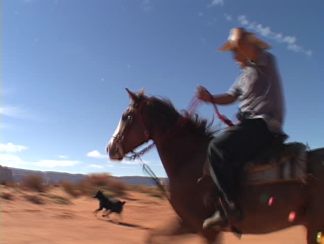 A cowboy on horseback rides fast across the Utah desert.