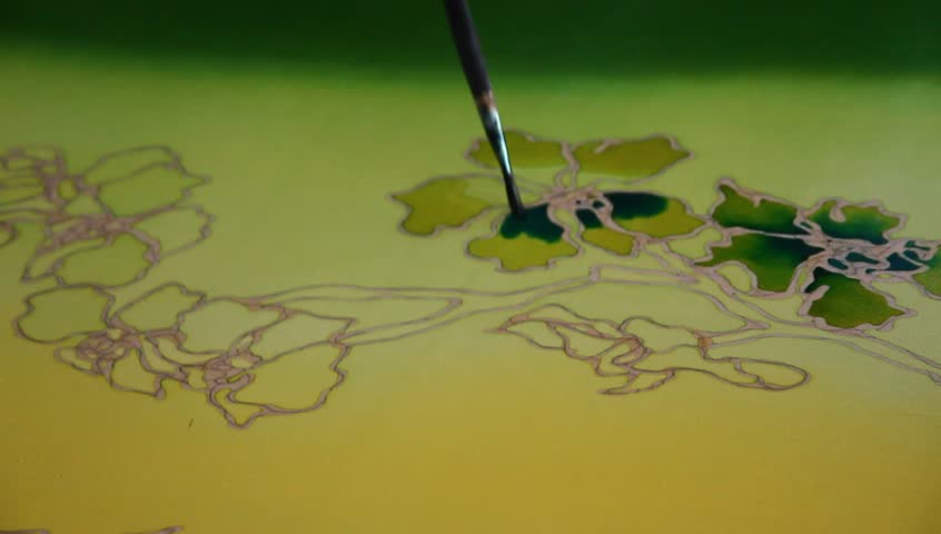 Close-up of an artist carefully paint the floral/flower motif on a yellow traditional batik fabric