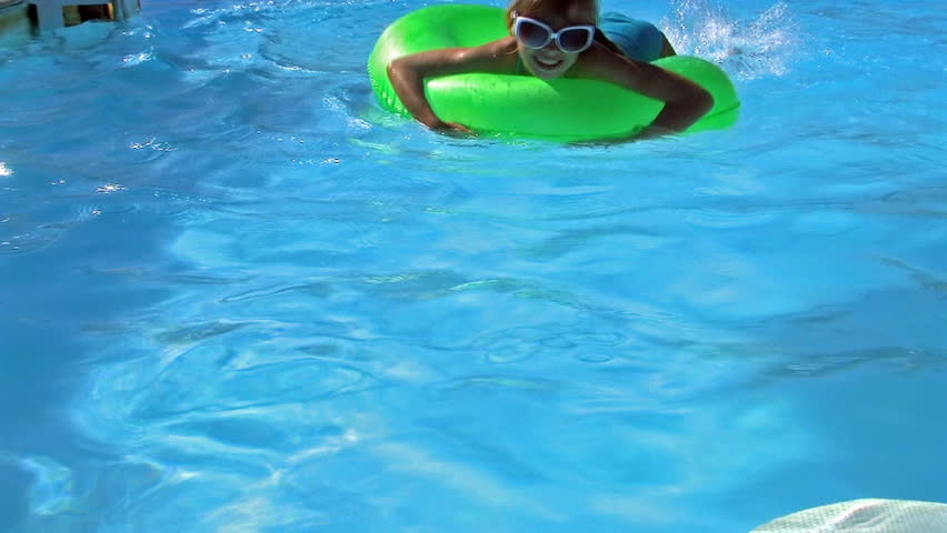 Children sitting on inflatable ring in swimming pool.