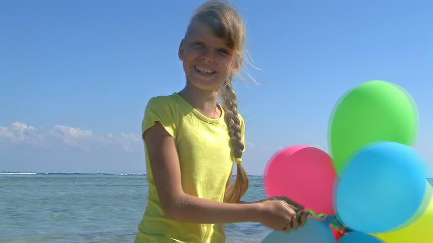 little girl playing with balloons at the beach.