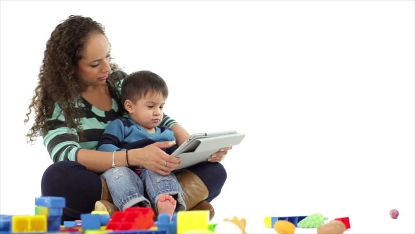 A pretty Hispanic mother keeps her cute little son interested in something on an electronic tablet. Taken on a white backdrop.