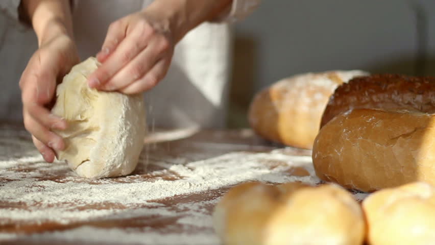 Baker kneading dough in flour on table, slow motion, dolly shot 