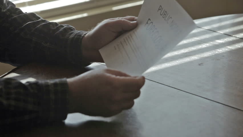 Foreclosure  public notice as man reads the court order while sitting at dark kitchen table. Upset and depressed over loss of his home. Tears court order up in frustration.