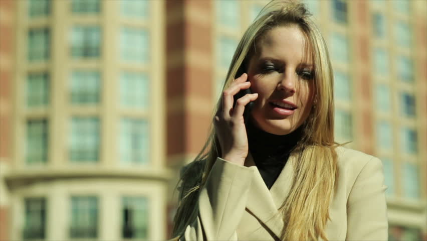 A pretty blond in business attire downtown on a breezy sunny day talks to someone on her cell phone.