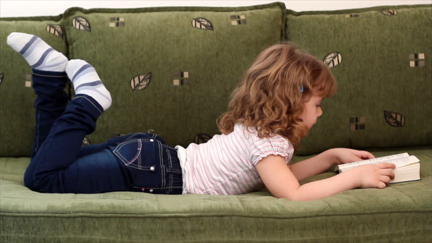 happy little girl lying on bed and reading a book