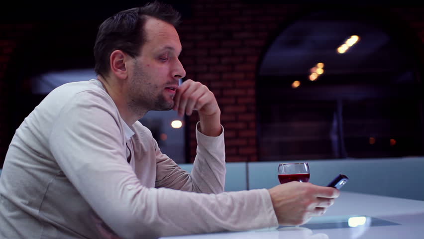 Sad lonely man drinking wine in bar and looking at cellphone