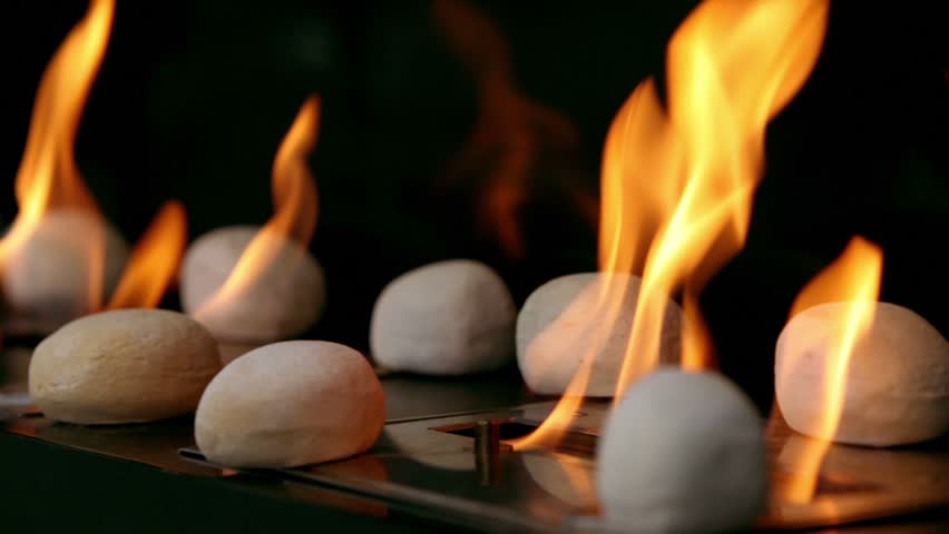 Tongues of flame go through slot in metal plate with round stones on it, closeup view
