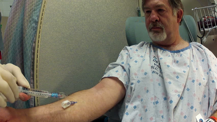 Medical nurse with patient intravenous catheter put into arm in preparation for a surgery procedure in a Veterans Hospital. Nurse feeling for a vein and inserting a needle. Man wearing hospital gown. 