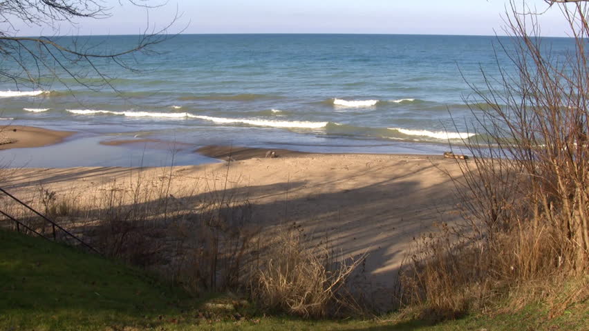Waves gently hit the beach, then recede as the sunlight reflects and glitters off of the water. (High Definition)