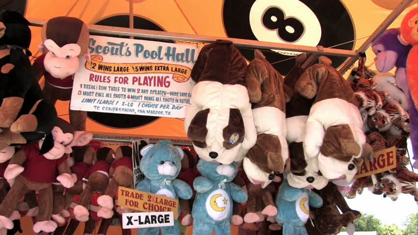 Stuffed animals in a tent at a carnival. Dogs, monkeys, bears and other colorful prizes. Pan left. Sign with rules of playing.