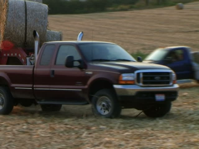 Close-up of trucks hauling round hay bales out of field - audio from external microphone. 