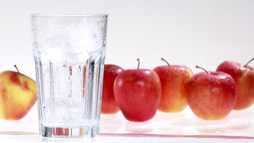 Pouring apple juice into a glass of ice cubes