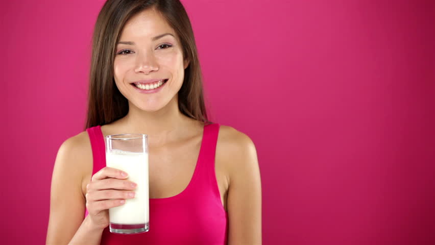 Woman drinking milk. Happy smiling girl drinking glass of water smiling looking at camera and side on pink background. Beautiful young mixed race Asian / Caucasian female model.