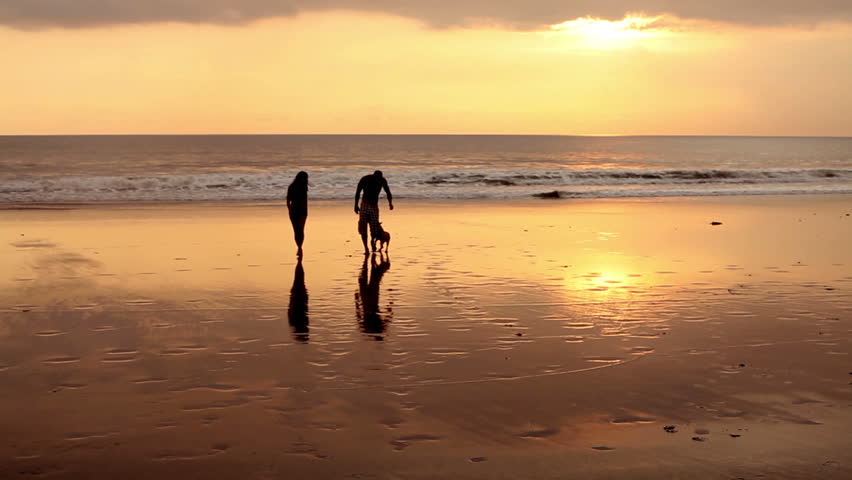 Couple walking on beach with dog at sunset in Bali