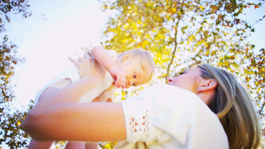 Blonde young mother and baby laughing together while playing outdoors