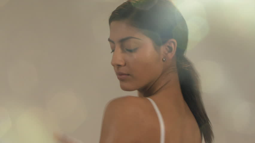 MEDIUM CLOSE UP PAN OF A YOUNG WOMAN MOISTURIZING HER BODY