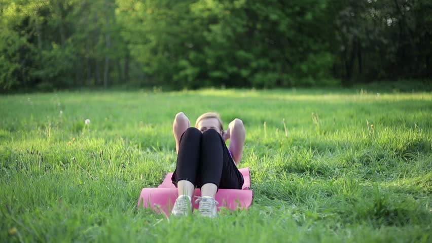 Woman in sport outfit doing sit ups in a park, tracking shot