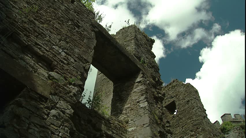 Sunlight and shadow on Irish castle wall ruins as camera, looking up past edges of walls pans around, through soft billowy clouds