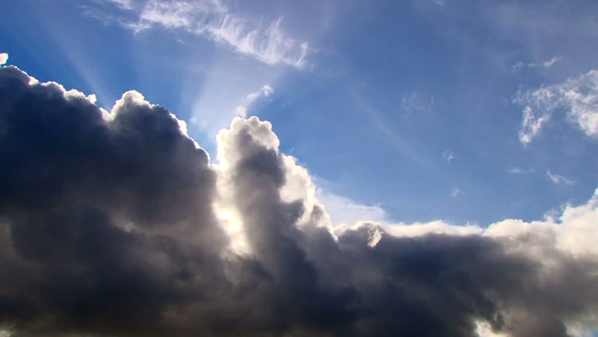 Beautiful cloudscape with large, building clouds and sunset behind shining sun rays and eventually breaking through cloud mass.