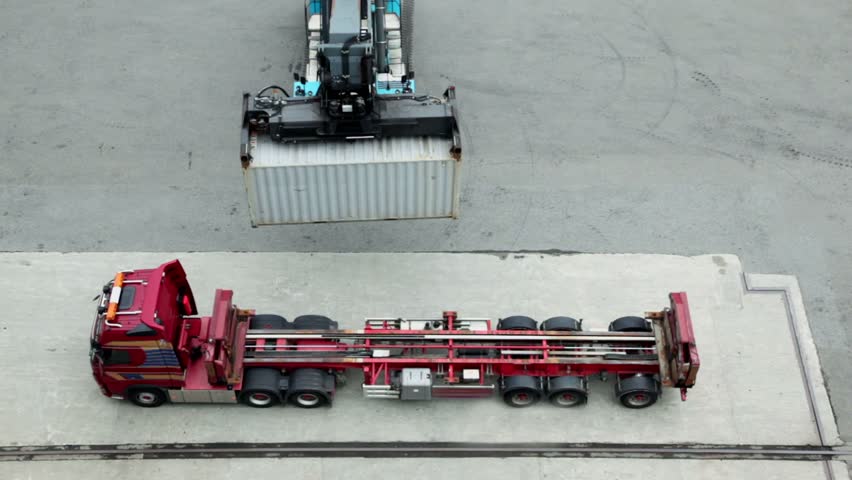 Crane moves and loads container to truck, view from above