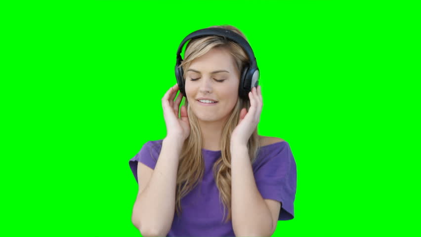 A woman moving to the music on her headphones in front of a green background