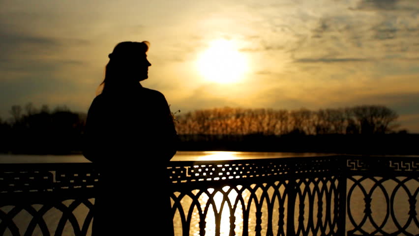 silhouette of pretty lady with flower that lean on railings near clear lake, sunset