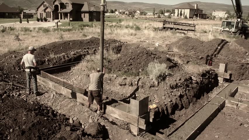 Construction workers prepare and pour the footings of a house.