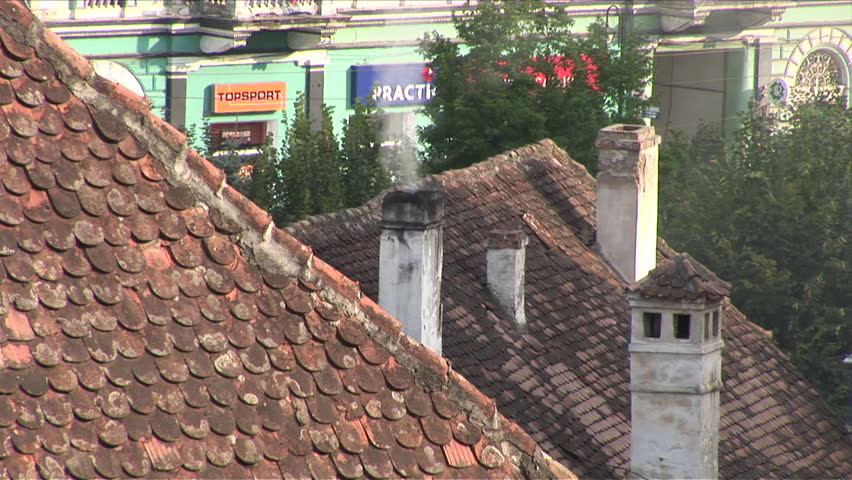 Sighisora, Romania - CIRCA July, 2006: Close view of a chimney spewing smoke next to other roofs