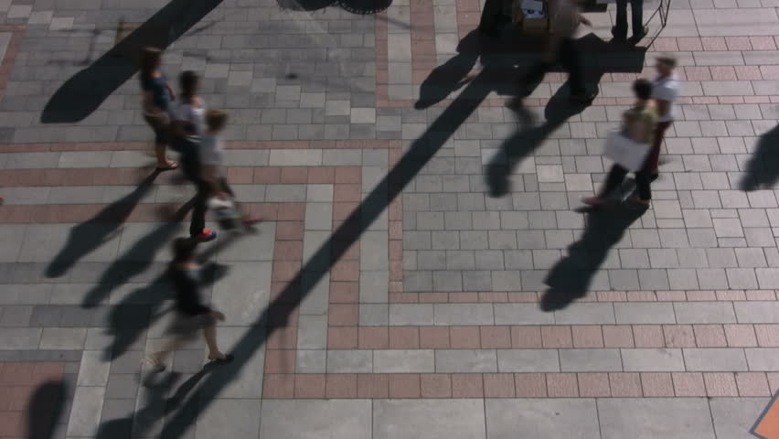 Time lapse aerial shot of people walking on city plaza with shadows 