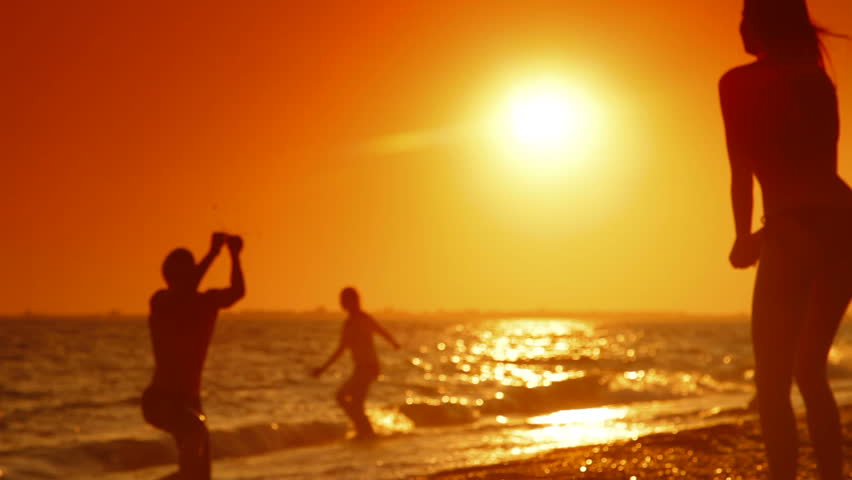 Young couple playing volleyball on the summer beach at sunset