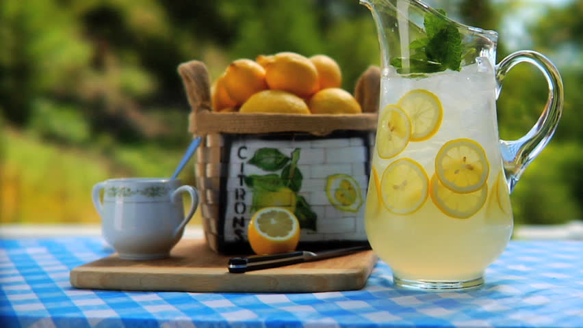 Man placing 2 glasses of lemonade by Pitcher of lemonade on table outside