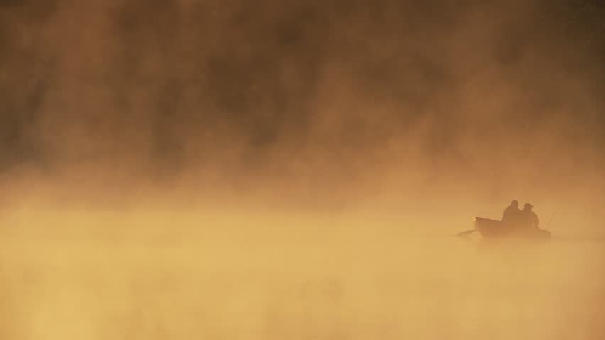 Fog rising from small pond at daybreak with men in small fishing boat 