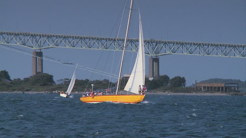 Classic America's Cup yacht with golden hull crossing Narragansett bay with Newport Bridge
