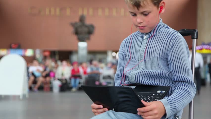 Little boy hold netbook when sits on travelling bag at train station