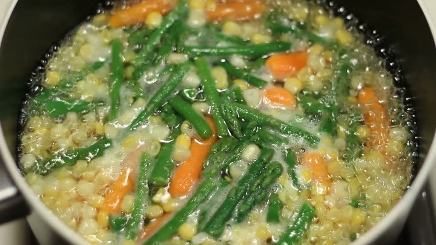 A colorful variety of vegetables carrots, asparagus, yellow and white corn boiling in a pan on the stove top for dinner.