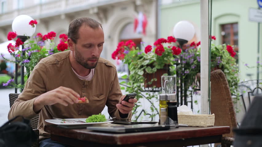 Young man with cellphone eating lunch in cafe
