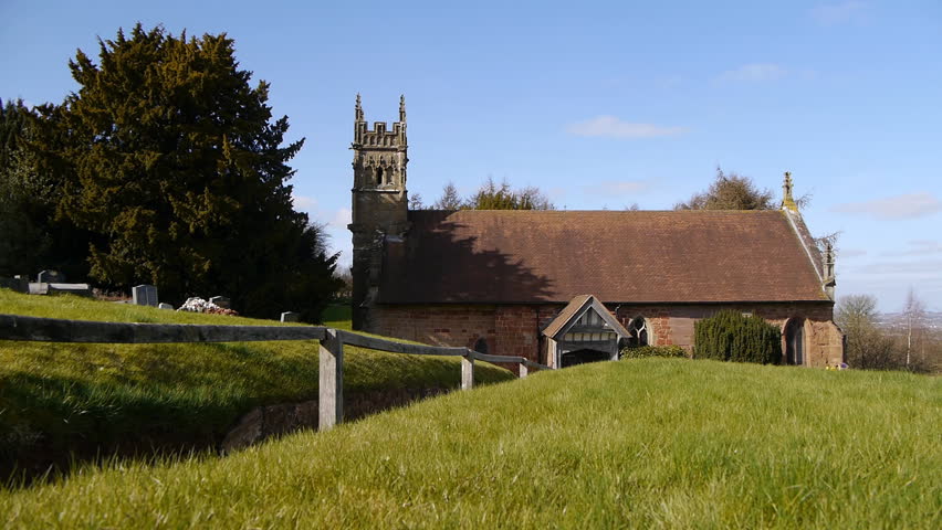 A small church on a sunny day with a clear blue sky and a big tree. Camera tracks past some grass in front of the church.