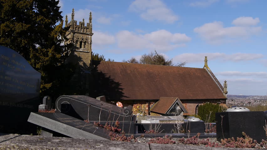 A small church on a sunny day. Camera tracks past some gravestones with the church in the background.