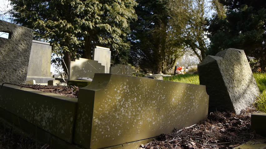 Camera tracks past some tumble-down graves and gravestones.