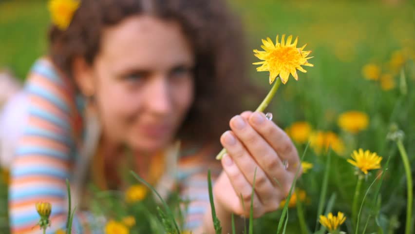 Young beautiful woman lies on lawn with dandelion in hand