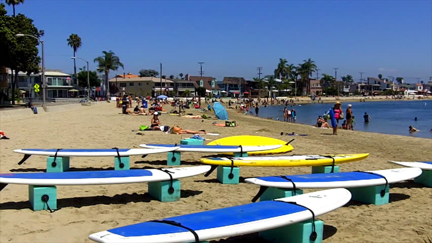 Paddle board surfboards (aka long boards) on the beach in Alamitos Bay in Long Beach, CA. In the distance, swimmers and sun bathers can be seen. 