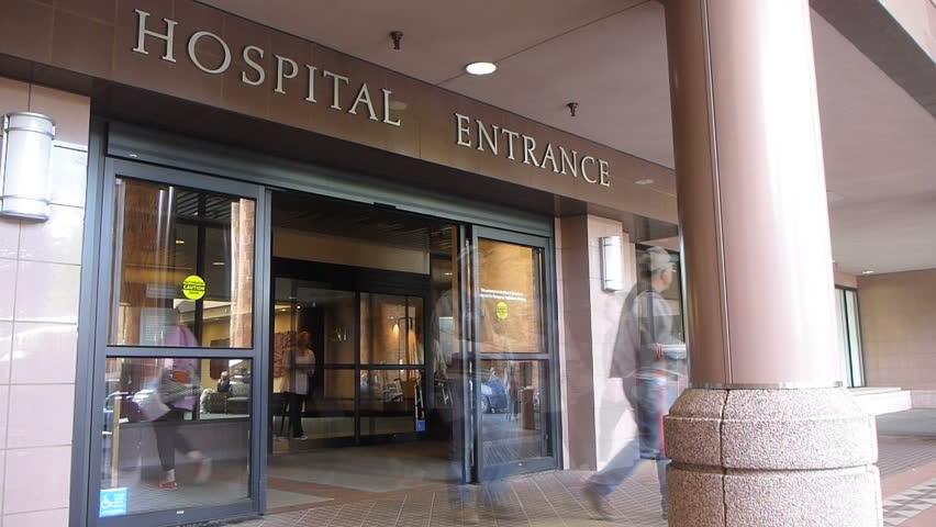 Time lapse effect at hospital entrance with patients entering and exiting through front door.