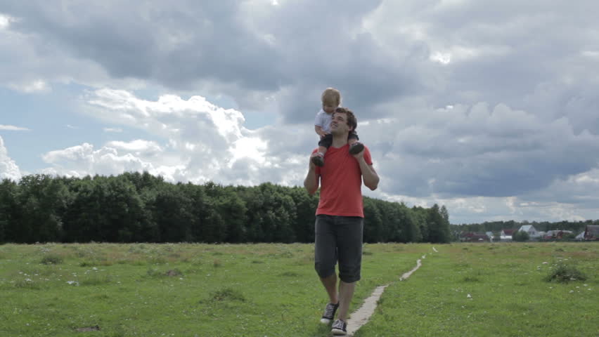 Young happy thirty year old father with his son on his shoulders walking across the field and kissing him.