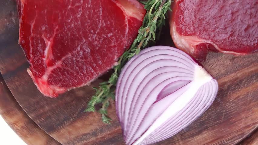uncooked raw beef fillet with thyme twig on wooden plate isolated over white background