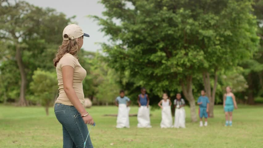 Young people and leisure activities, teacher and group of school children having fun while playing sack race. Slow motion