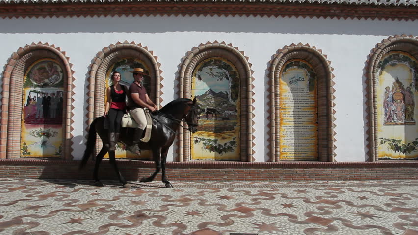 Man and woman riding a horse through a village in Andalusia, Spain