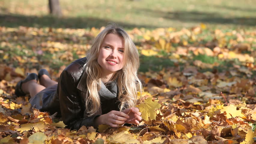 Pretty blonde lying on the fallen leaves in park catching the last glimpses of the autumn sun