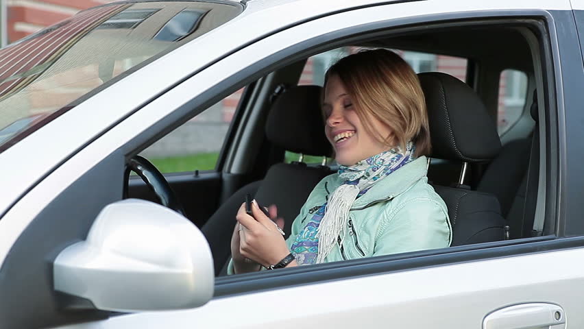 Woman sitting in new bought car, looking around, showing ignition key and waving hand in window