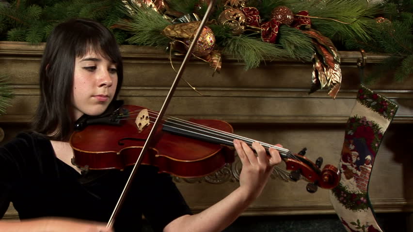 A lovely young girl playing on her viola in front of an elegantly decorated mantel