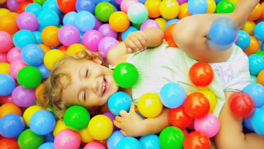 Cute blonde toddler lying on multi coloured plastic balls in big paddling pool shot on RED EPIC